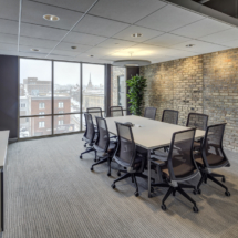 meeting-room-light-grey-striped-pattern-rug-area_brown-fabric-upholstered-meeting-chair_cream-stained-wooden-meeting-table_natural-silver-aluminium-frame-clear-glass-ventilation-window